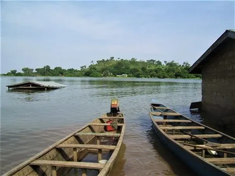 Destinations - Wooden canoes docked on the shore of Lake Volta near small floating houses and an island.